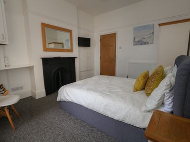 A bedroom with a bed with white bedding and yellow pillows a wooden door a black fireplace and a wall mirror at Flat 2 - Studland in Bournemouth