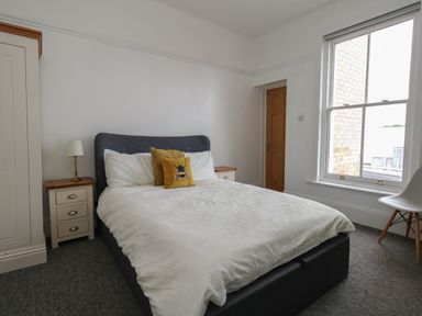 A bedroom with a double bed and white bedding two bedside tables with lamps a wardrobe a window and a chair at Flat 2 - Studland in Bournemouth