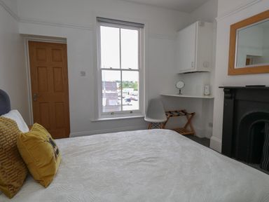 A bedroom with a bed, wooden door, window, chair, wall cabinet, and a fireplace at Flat 2 - Studland in Bournemouth
