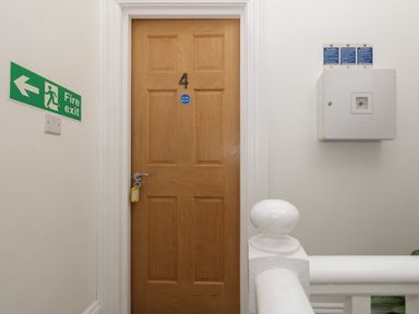 A wooden door numbered 4 in a hallway with fire exit sign and a white safety box at Flat 4 - Hengistdury in Bournemouth