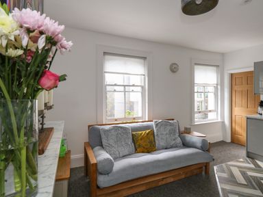 A sitting area with a grey sofa and cushions next to two windows with blinds at Flat 4 - Hengistdury in Bournemouth