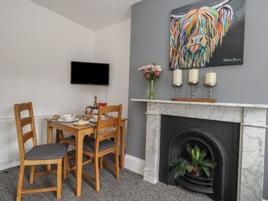A dining area with a wooden table and chairs a marble fireplace with candles and plants and a wall mounted television at Flat 4 - Hengistdury in Bournemouth