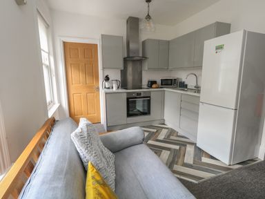 A kitchen with grey cabinets white appliances and a sofa with cushions at Flat 4 - Hengistdury in Bournemouth