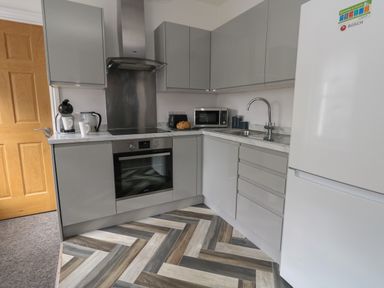 A kitchen with grey cabinets a refrigerator an oven a microwave a toaster a coffee machine a kettle and a sink at Flat 4 - Hengistdury in Bournemouth