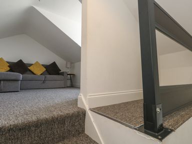 A grey sofa with cushions under a slanted ceiling next to a small side table with a lamp at Flat 4 - Hengistdury in Bournemouth