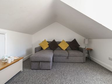 A grey sofa with yellow and brown cushions in a room with a sloped ceiling and a side table with a lamp at Flat 4 - Hengistdury in Bournemouth