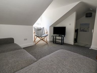 A living room with a gray sofa a folding chair a TV on a stand and sloped ceilings at Flat 4 - Hengistdury in Bournemouth