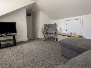 A living room with a television on a stand a gray chair a wooden chest with tea set and pastries and a gray sofa at Flat 4 - Hengistdury in Bournemouth