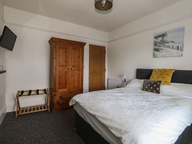 A bedroom with a double bed two pillows a wooden wardrobe a wooden door a wall-mounted TV and a luggage rack at Flat 4 - Hengistdury in Bournemouth