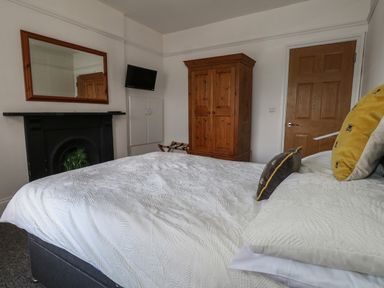A bedroom with a bed with pillows a wooden wardrobe a wall-mounted television a mirror above a black fireplace and a wooden door at Flat 4 - Hengistdury in Bournemouth