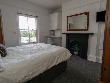 A bedroom with a bed a window a desk with a chair a fireplace with a plant inside a wall mirror and a wall-mounted TV at Flat 4 - Hengistdury in Bournemouth