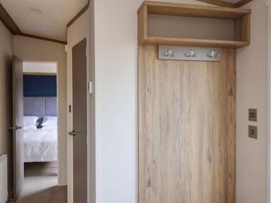A hallway with a wooden coat rack and doors leading to a bedroom with a bed at Hazel Lodge in Whitby
