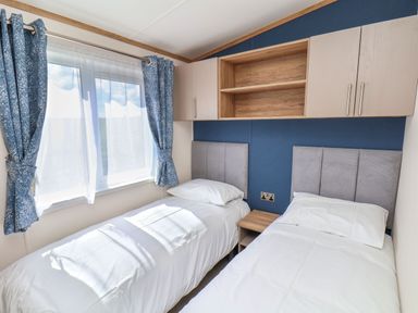 A bedroom with two single beds a nightstand between them blue curtains on a window and built in cabinets above at Hazel Lodge in Whitby