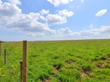 A grassy field with a wooden post and wire fence under a blue sky with clouds at Juniper Lodge in Whitby