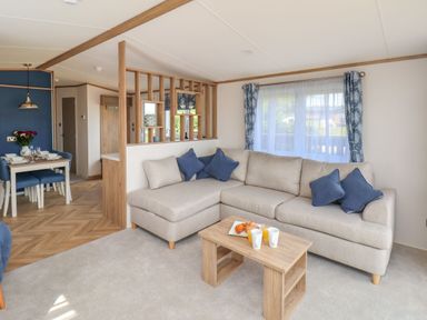 A living room with a beige sectional sofa and blue pillows next to a wooden coffee table with drinks and pastries at Juniper Lodge in Whitby