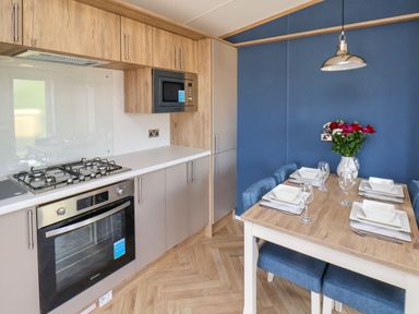 A kitchen with a gas stove oven microwave and a dining table set with plates glasses and flowers at Juniper Lodge in Whitby