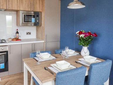 A dining table set with plates bowls glasses and cutlery next to a kitchen area with microwave oven and food items at Juniper Lodge in Whitby