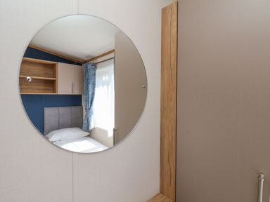 A reflection in a round mirror of a bedroom with a bed a window with curtains and overhead cabinets at Willow Lodge in Whitby