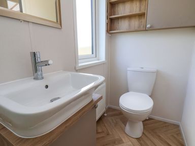 A bathroom with a white sink and faucet next to a white toilet under a window at Willow Lodge in Whitby