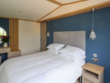 A bedroom with a bed white bedding bedside tables pendant lights and a dresser with a round mirror and flowers at Willow Lodge in Whitby