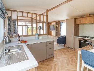 A kitchen and living area with a wooden divider a blue chair a mounted television and kitchen appliances at Magnolia Lodge Whitby