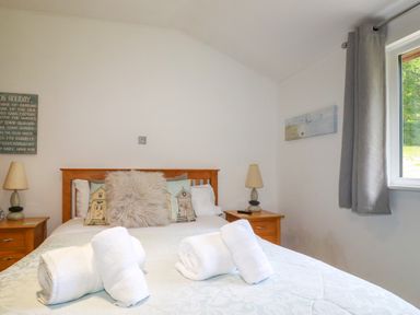 A bedroom with a double bed two bedside tables with lamps window with gray curtains at 3 Lake View in Lanreath