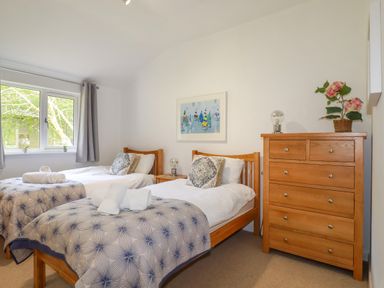 A bedroom with two single beds a wooden chest of drawers and a window at 3 Lake View in Lanreath
