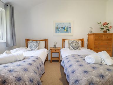 A bedroom with two single beds a bedside table with a lamp a chest of drawers and a framed picture on the wall at 3 Lake View in Lanreath