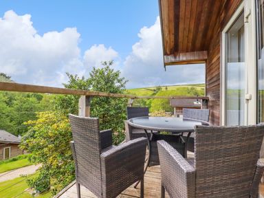 A balcony with wicker chairs and a round table overlooking trees and hills at 3 Lake View in Lanreath