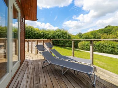 A wooden deck with two lounge chairs overlooking a grassy area and trees at 1 Hedgerows in Lanreath