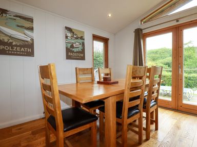A dining room with a wooden table and six chairs near glass doors at 1 Hedgerows in Lanreath