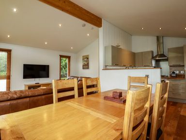 A dining area with wooden chairs and table adjacent to a living room with leather sofas and a wall-mounted television at 1 Hedgerows in Lanreath