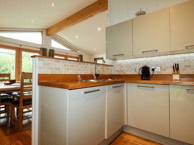 A kitchen with wooden countertops cabinets and a dining area beyond with wooden chairs at 1 Hedgerows in Lanreath