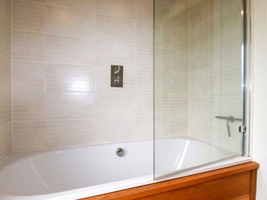 A bathtub with a glass shower screen and tiled walls at 1 Hedgerows in Lanreath