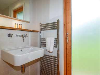 A bathroom sink with wall-mounted faucet a towel on a heated rail and a frosted glass door at 1 Hedgerows in Lanreath