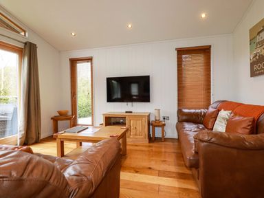 A living room with leather sofas a wooden coffee table a wall-mounted television and wooden blinds at 1 Hedgerows in Lanreath