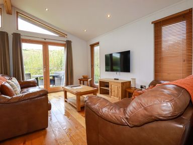 A living room with two leather sofas a wooden coffee table a wall-mounted TV and patio doors at 1 Hedgerows in Lanreath