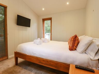 A bedroom with a bed with white linens and an orange pillow two windows with blinds and a wall mounted television at 1 Hedgerows in Lanreath