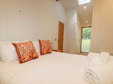 A bedroom with a bed with floral pillows and folded towels near a wooden door and window at 1 Hedgerows in Lanreath