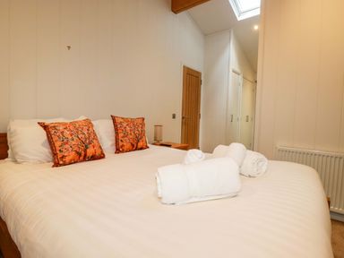 A bedroom with a bed with white linens and orange pillows next to a wooden door at 1 Hedgerows in Lanreath