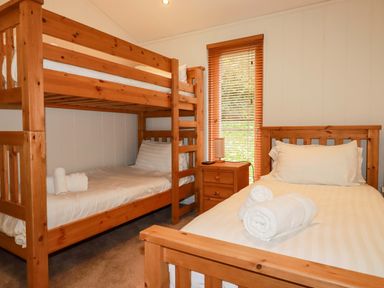 A bedroom with wooden bunk beds a single wooden bed a bedside table with a lamp and window blinds at 1 Hedgerows in Lanreath