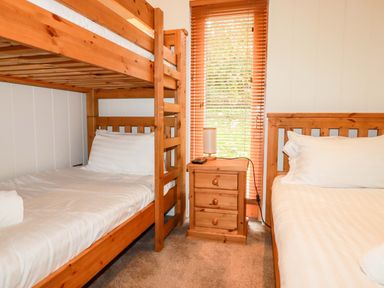 A bedroom with wooden bunk beds a wooden single bed a wooden nightstand with a lamp and a window with blinds at 1 Hedgerows in Lanreath