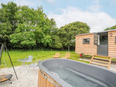 An outdoor area with a hot tub a small table with two chairs two wooden lounge chairs and a wooden cabin at Bracken Broad Langdon near Wainhouse Corner