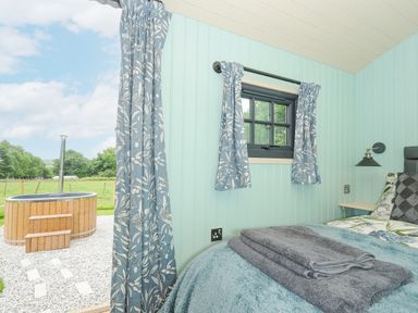 A small bedroom with a bed and folded towels by a window and an outdoor wooden hot tub at Bracken in Broad Langdon near Wainhouse Corner