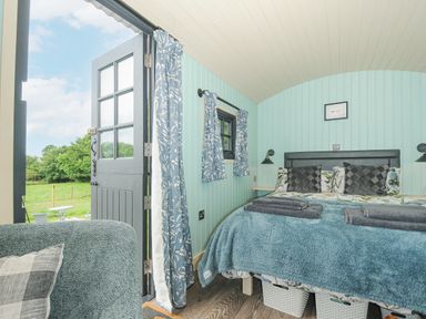 A bedroom with a double bed blue bedding and floral cushions next to an open door with blue floral curtains at Bracken Broad Langdon near Wainhouse Corner