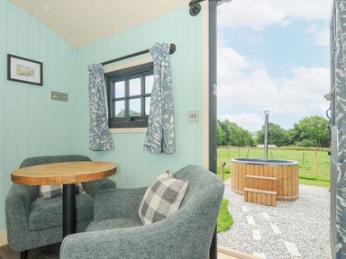 A small seating area with two armchairs and a round wooden table next to a window and an open door showing a wooden hot tub outside at Bracken Broad Langdon near Wainhouse Corner