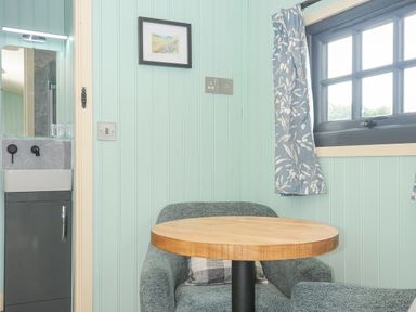 A small seating area with an armchair a round wooden table a window with floral curtains and a small sink with a mirror at Bracken Broad Langdon near Wainhouse Corner