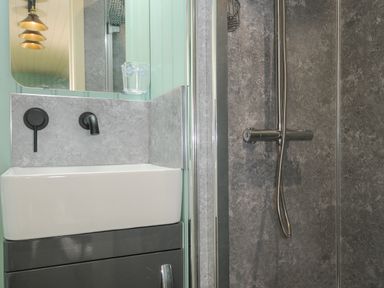 A bathroom with a white sink, black faucet, mirror, glass cup, and a shower with a handheld showerhead at Bracken Broad Langdon near Wainhouse Corner