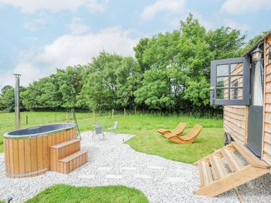 An outdoor area with a wooden hot tub patio furniture and wooden lounge chairs near a wooden building at Bracken Broad Langdon near Wainhouse Corner