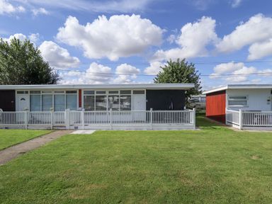 A single story house with a white fence and green lawn under a blue sky at 68 Cherry Park in Chapel St Leonards